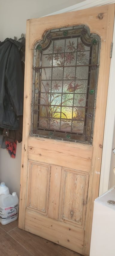 Wooden door with decorative stained glass panel and rustic finish.